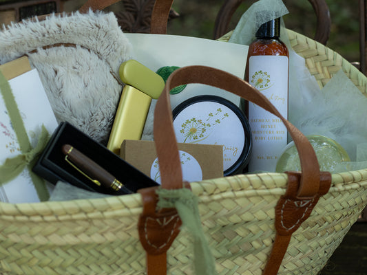 Close-up of a woven gift tote with body butter, lotion, stationery, a pen, and soft comfort items arranged inside.
