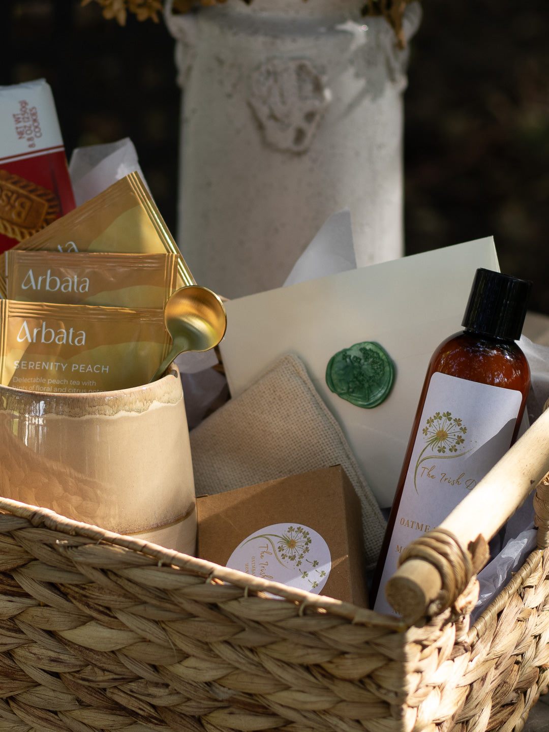 A Little Kindness gift basket with tea, biscuits, mug, soap, lotion, stationery, and small comfort items arranged outdoors on a round table.