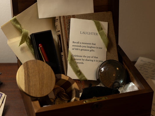 Close-up of the Letters & Legacy gift with a “Laughter” writing prompt, pen, magnifier, ribbon-tied journal, wax seal pieces, and wooden keepsake box.