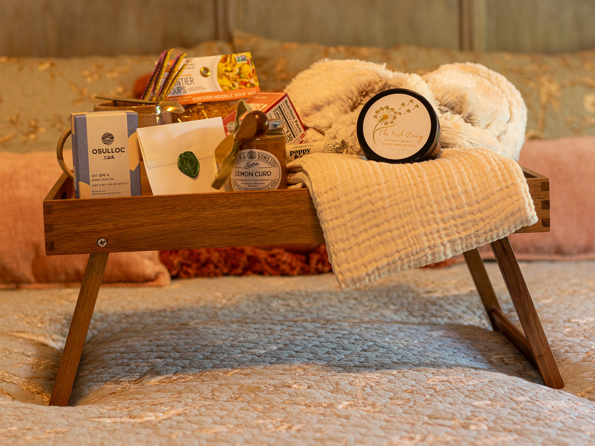 Rest & Restore gift arranged on a wooden bed tray with tea, soup, lemon curd, body butter, soft blanket, and comforting care items.