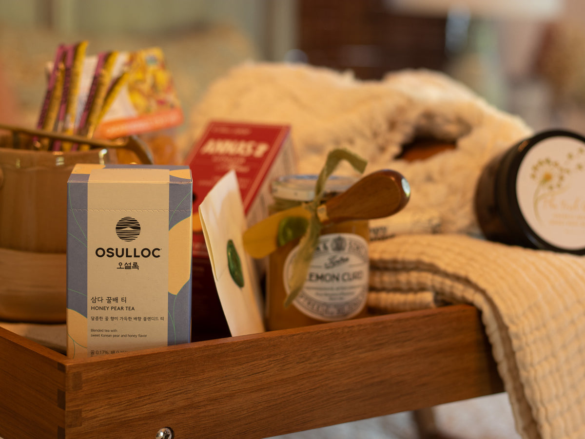Close-up of the Rest & Restore gift featuring honey pear tea, lemon curd, a handwritten note, body butter, and soft comfort items.