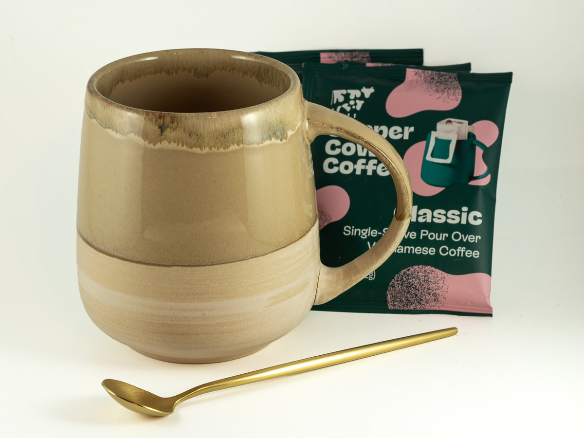 Ceramic mug with single-serve pour-over coffee packets and gold spoon