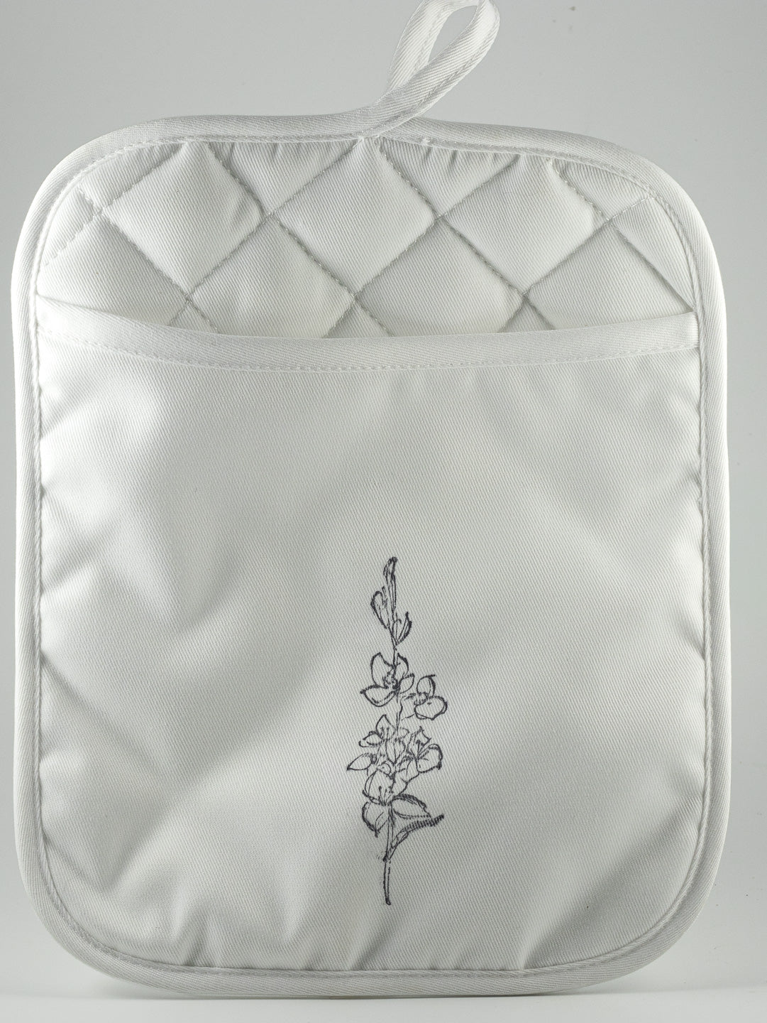 A white quilted pot holder with a small hand-stamped botanical image on the front, featuring a top hanging loop and a front pocket.