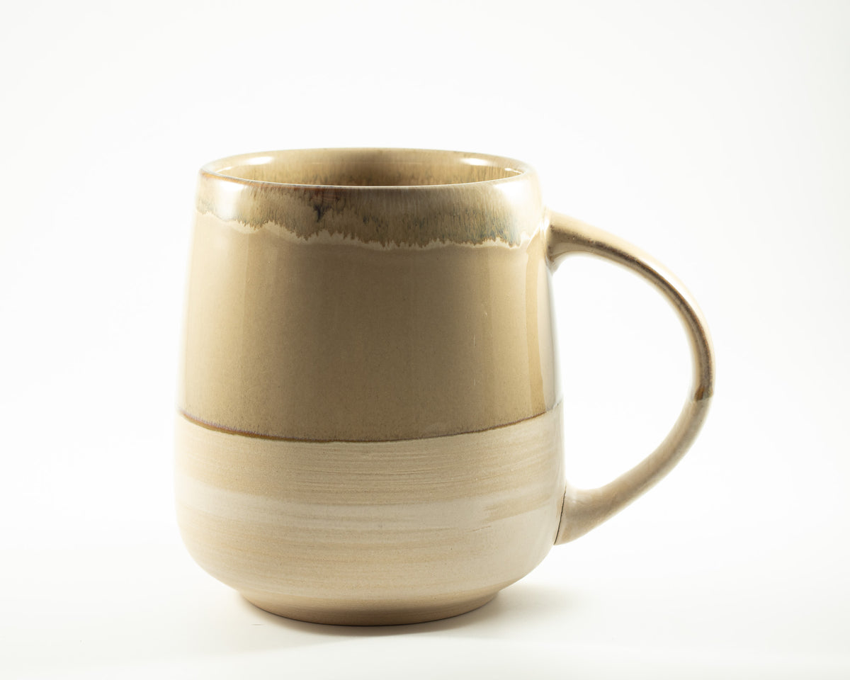 A handmade ceramic mug with a two-tone beige and light brown glaze, featuring a rustic dripping edge on the rim and a curved handle, part of the Irish Daisy gift collections. 
