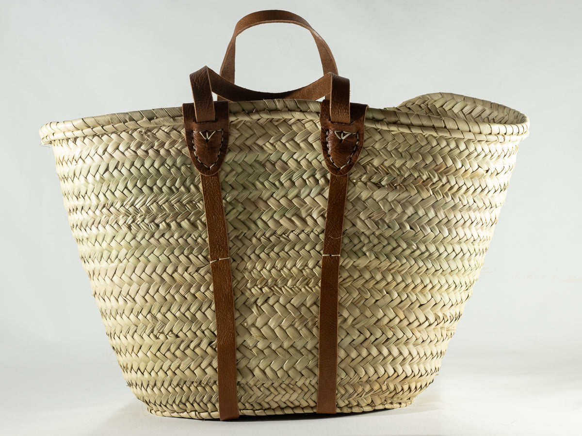 Natural woven French market basket with brown leather handles and vertical leather straps.