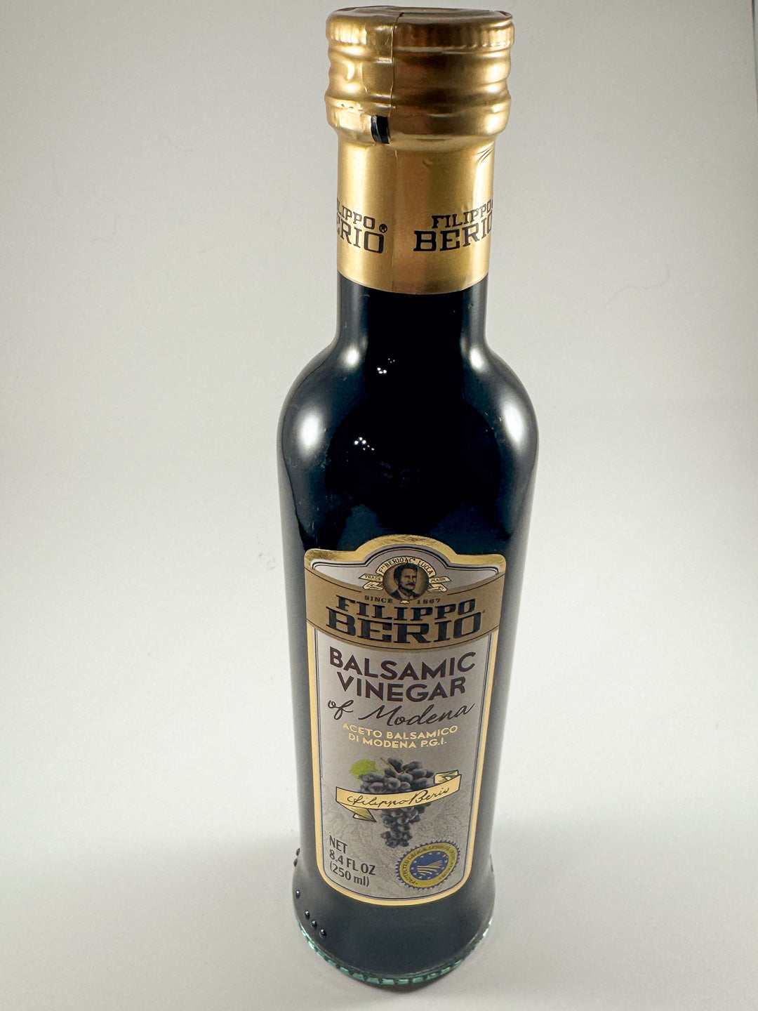 Bottle of Filippo Berio balsamic vinegar of Modena with gold foil neck and cream label.