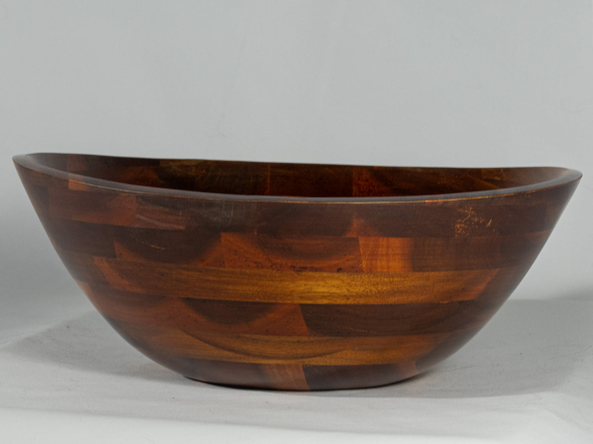 Large dark wood serving bowl with warm patchwork grain and a wide shallow shape.