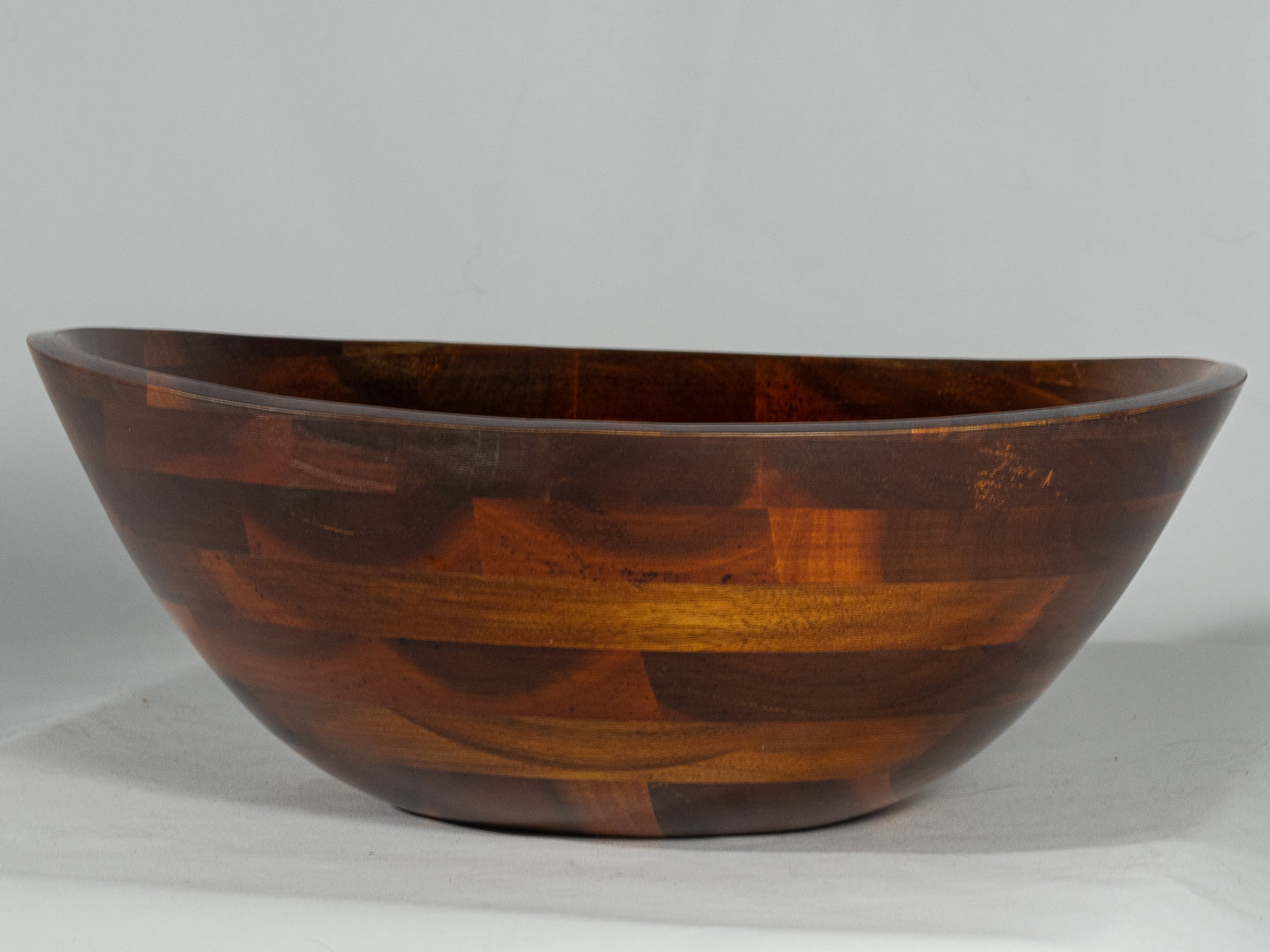 Large dark wood serving bowl with warm patchwork grain and a wide shallow shape.