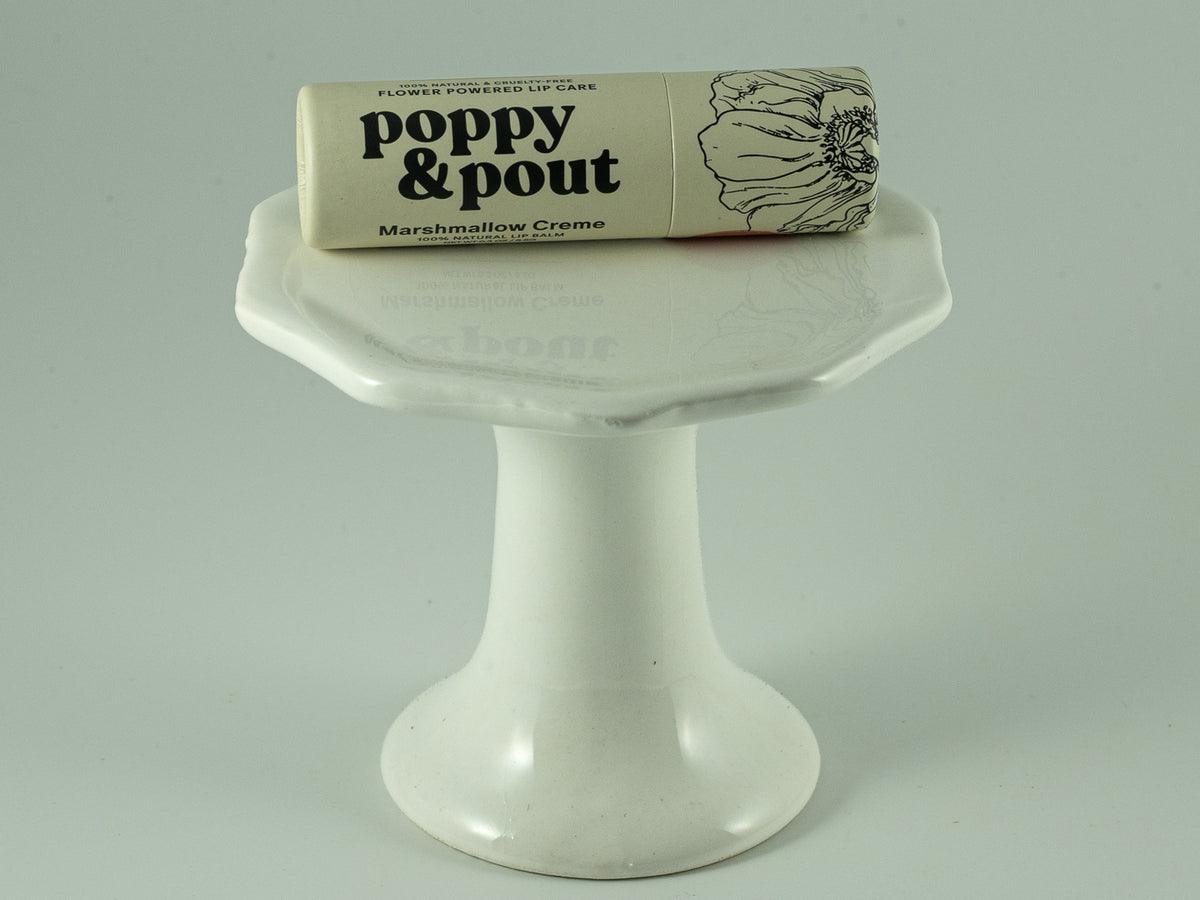 Poppy & Pout Marshmallow Creme lip balm resting on a small white pedestal dish.