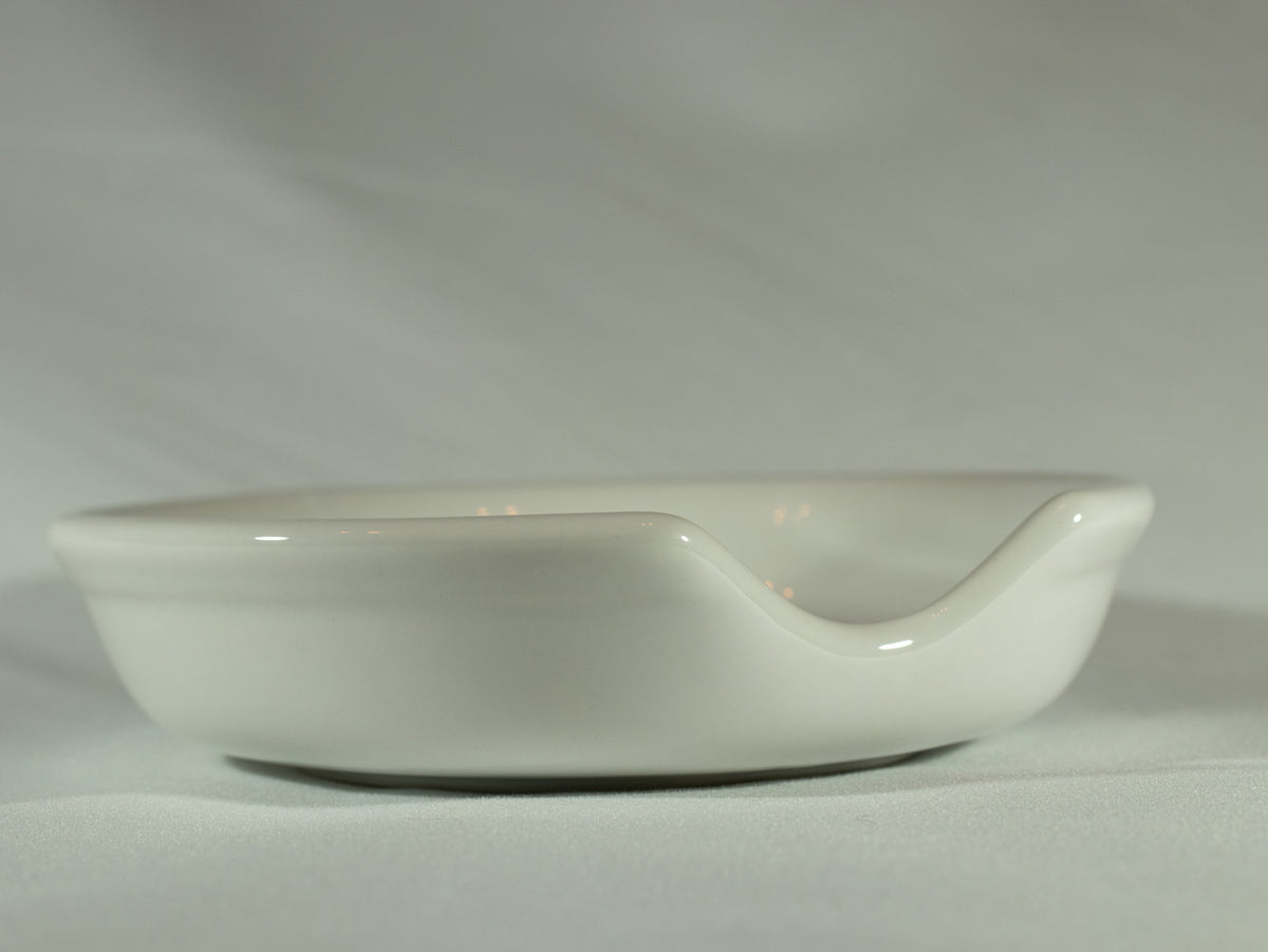 White ceramic spoon rest with a curved notch, photographed on a soft neutral background.