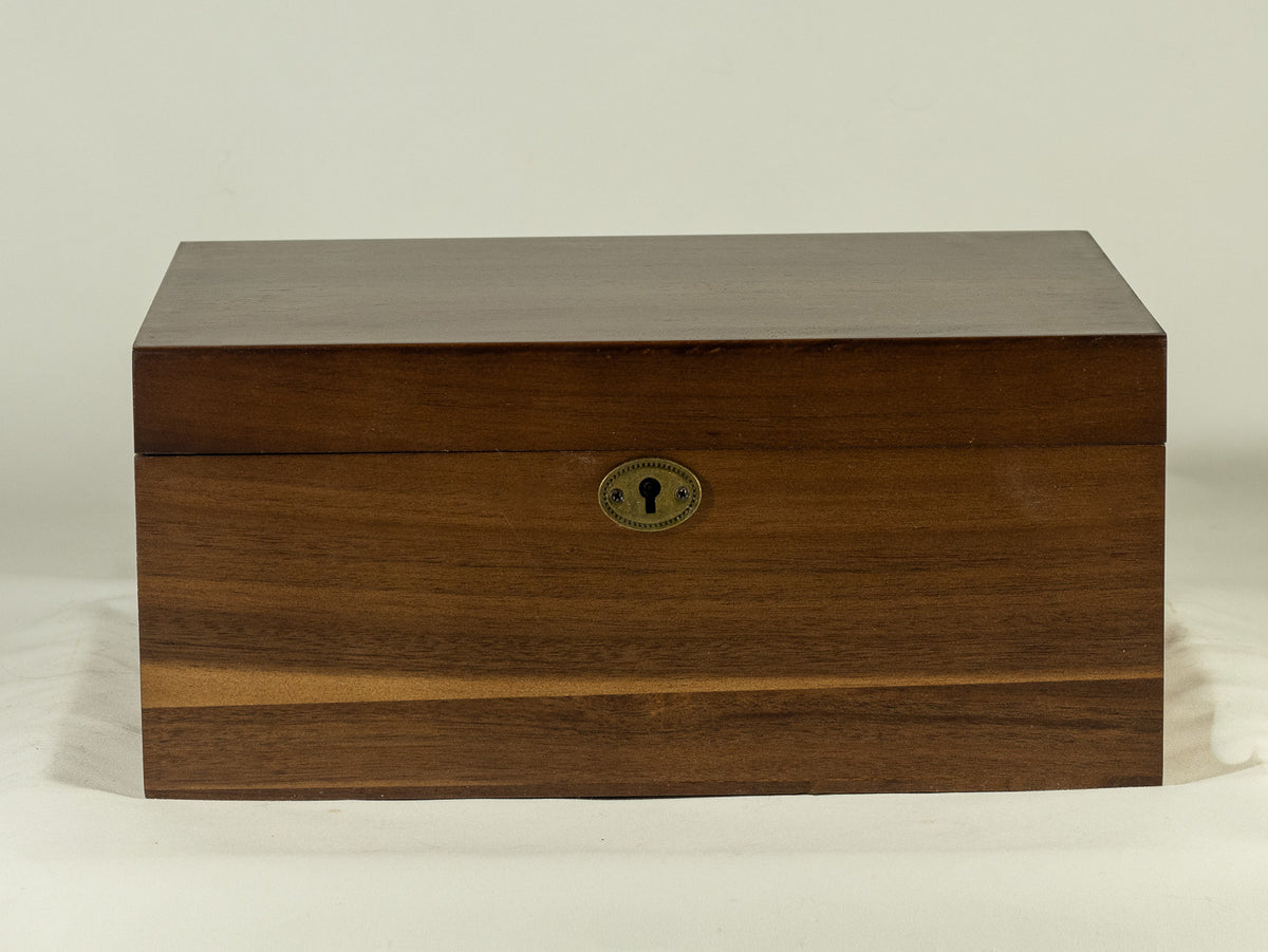 Warm wood keepsake box with brass keyhole lock (with key) and natural grain detail, photographed on a soft neutral background.